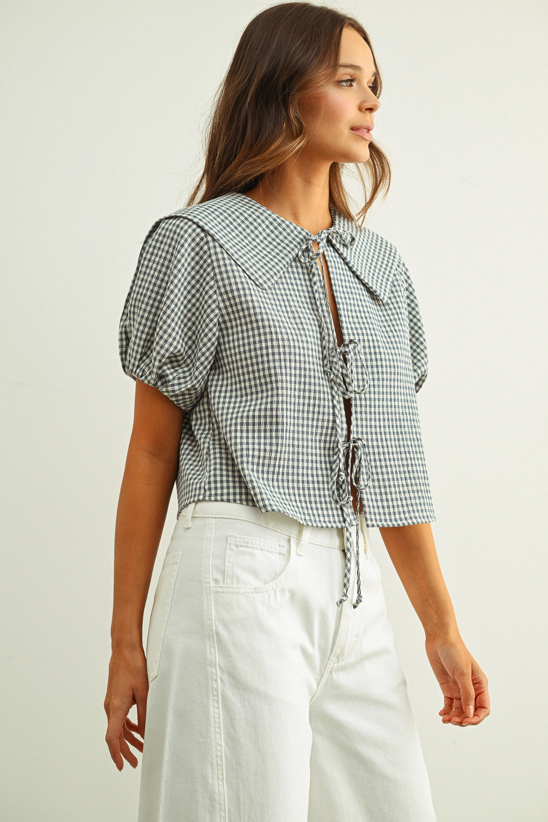 Woman wearing a checkered blouse with puff sleeves and white pants on a plain background