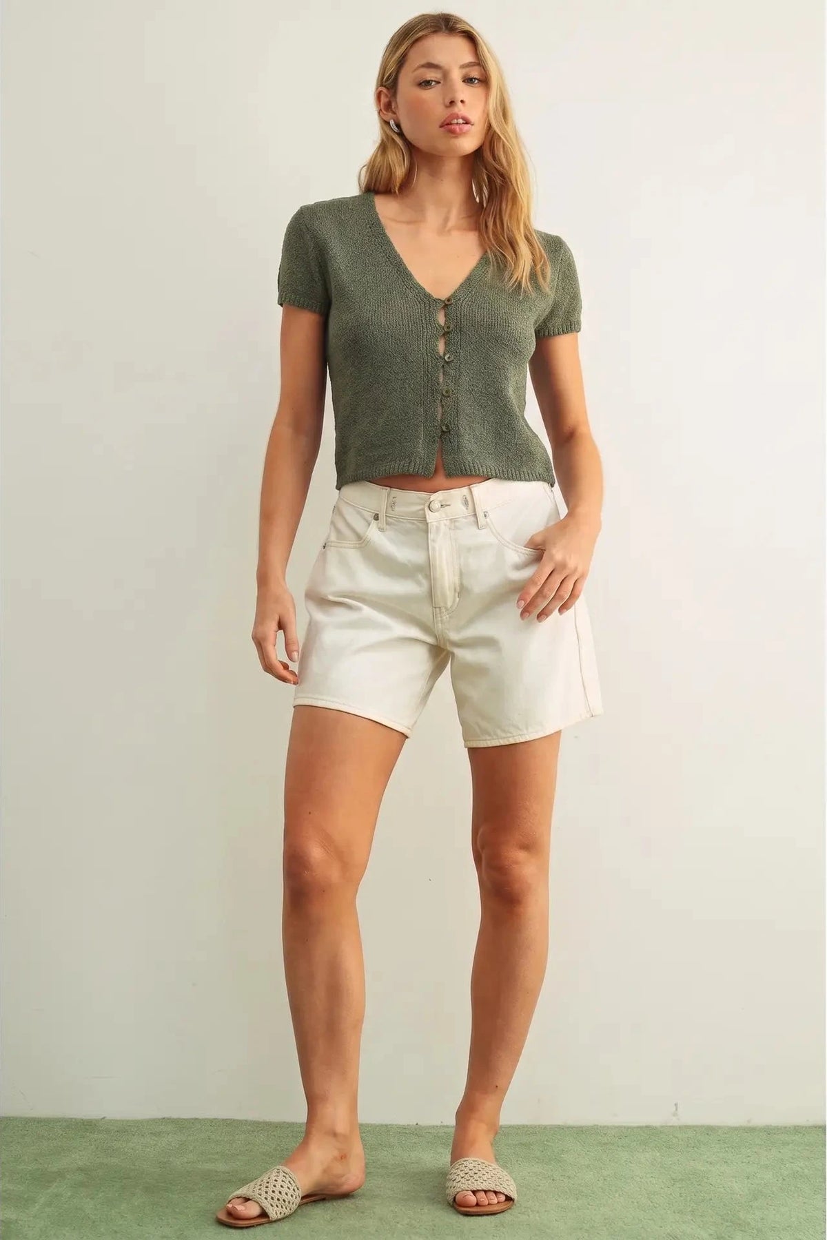 Woman wearing a green cropped top and white shorts on a plain background