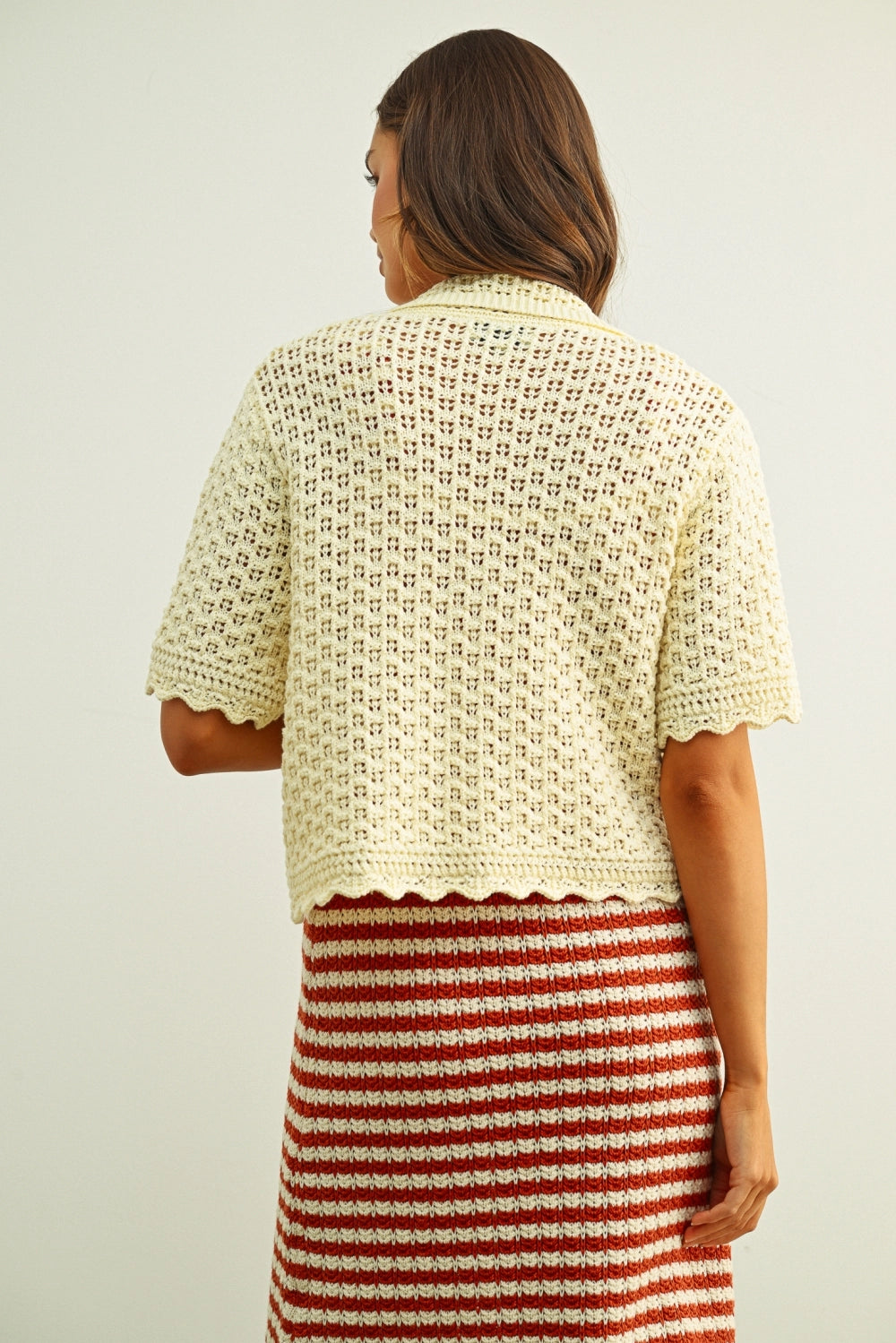 Woman wearing a patterned top and striped skirt against a plain background
