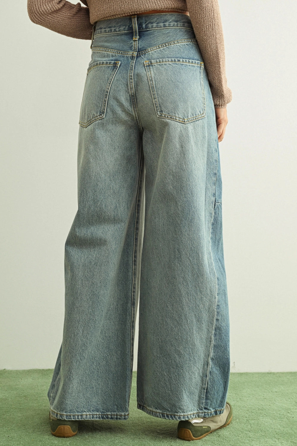 Wide-leg jeans worn by a person on a green and beige background