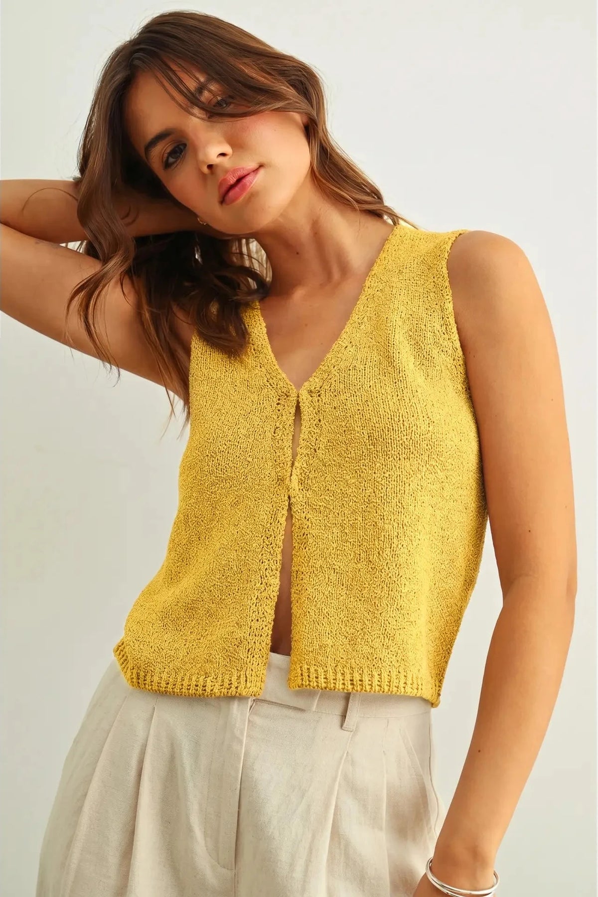 Woman wearing a yellow knitted vest against a plain background