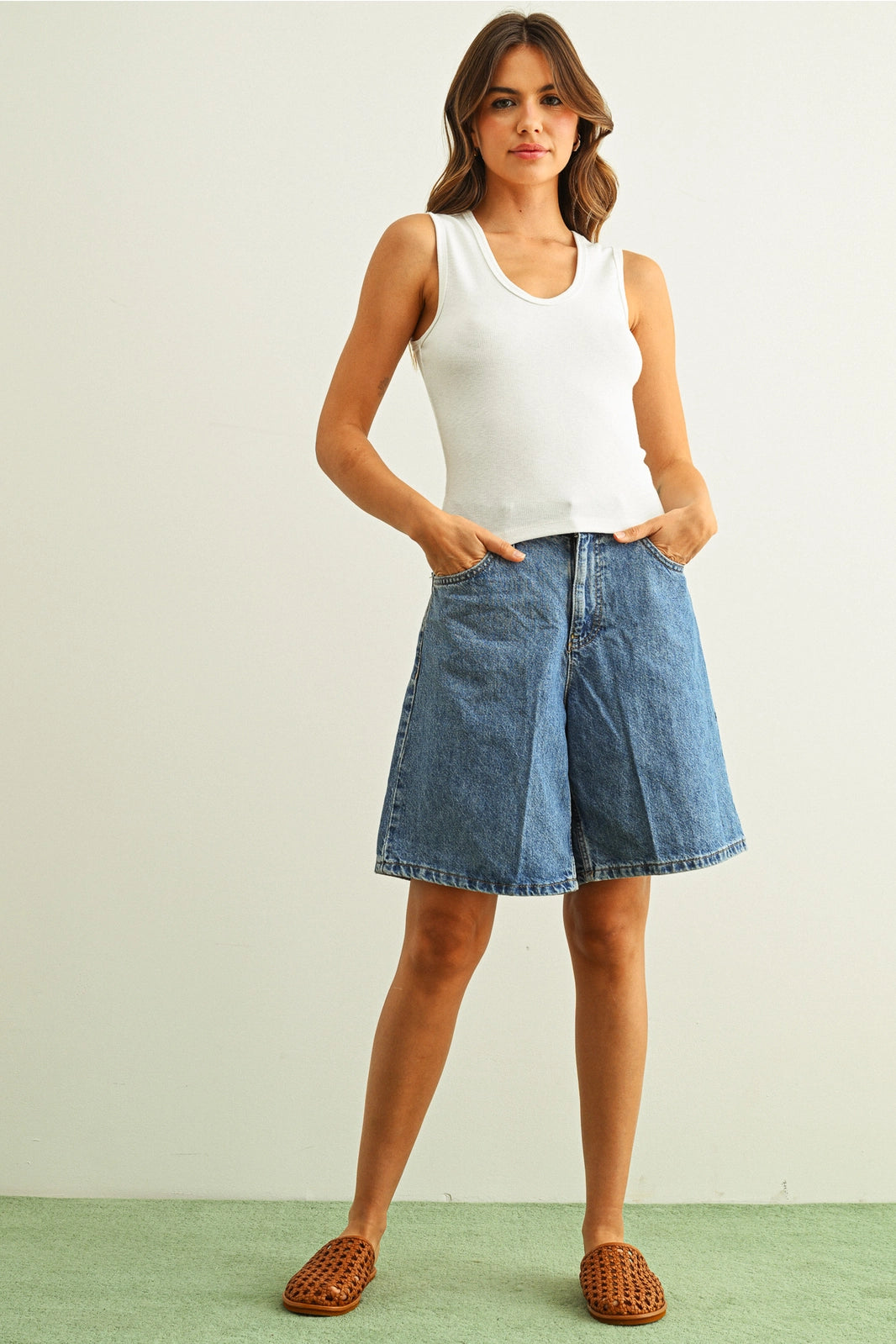 Woman wearing a white tank top and blue denim skirt on a plain background