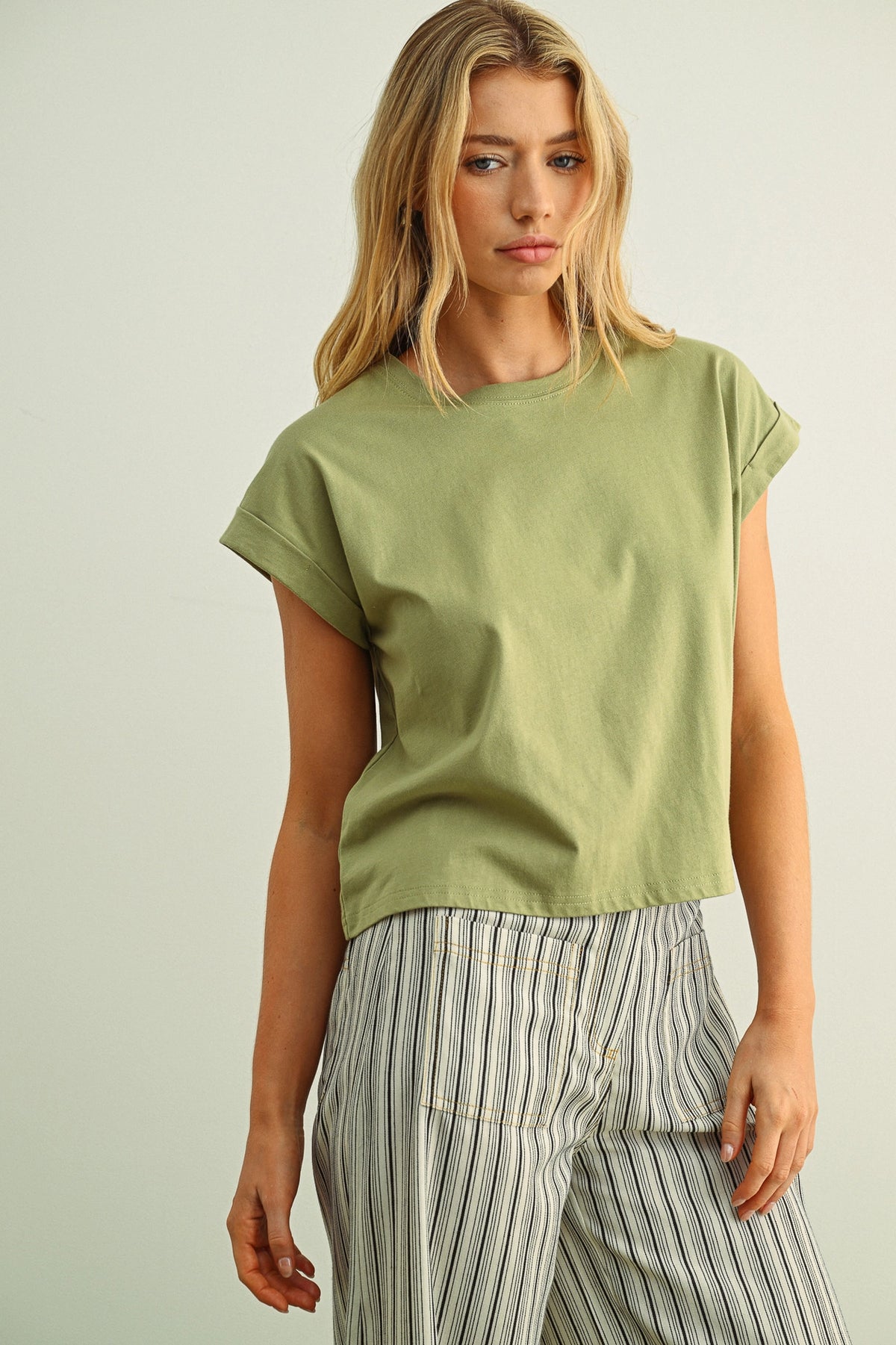 Woman wearing a green t-shirt and striped pants against a plain background