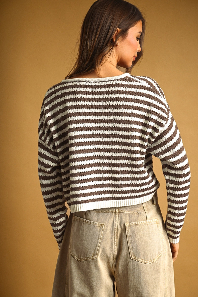A woman shown from the back wearing a brown and white horizontally striped knit sweater and light beige jeans, set against a solid warm tan background.