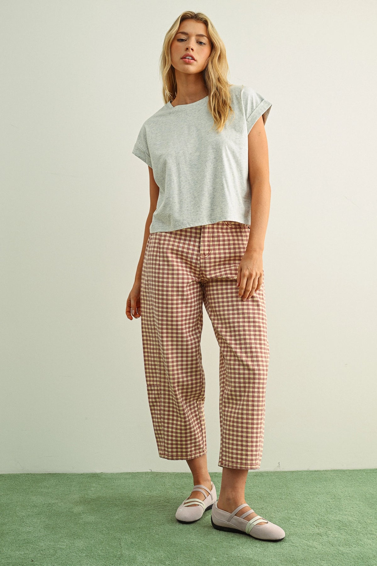 Woman wearing a light gray t-shirt and checkered pants on a green floor with a white wall background