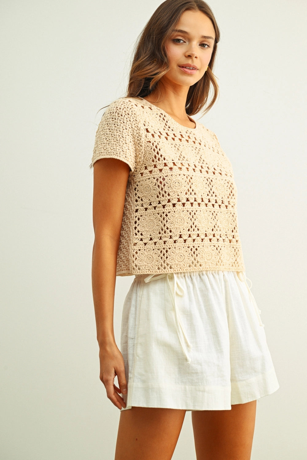 Woman wearing a beige crochet top and white shorts on a light background
