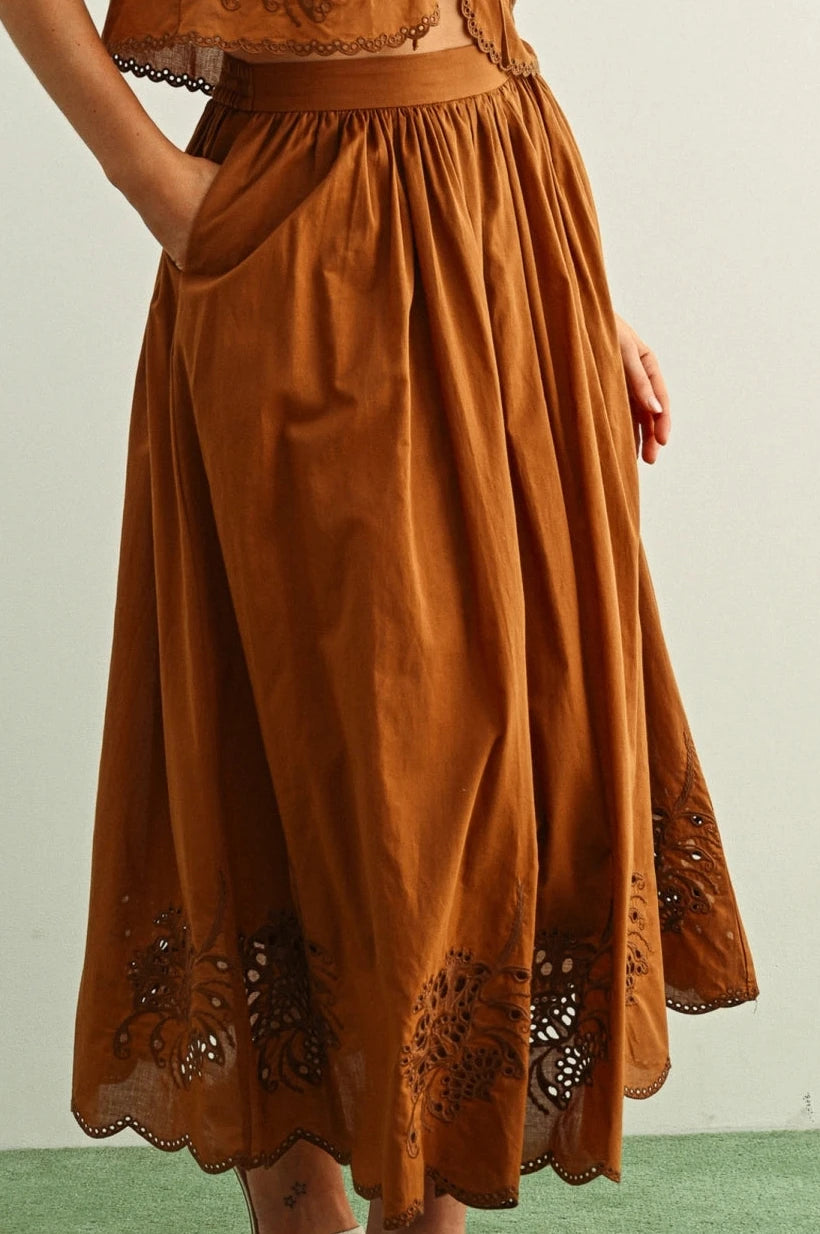 Brown embroidered dress worn by a person on a green floor with a white wall background