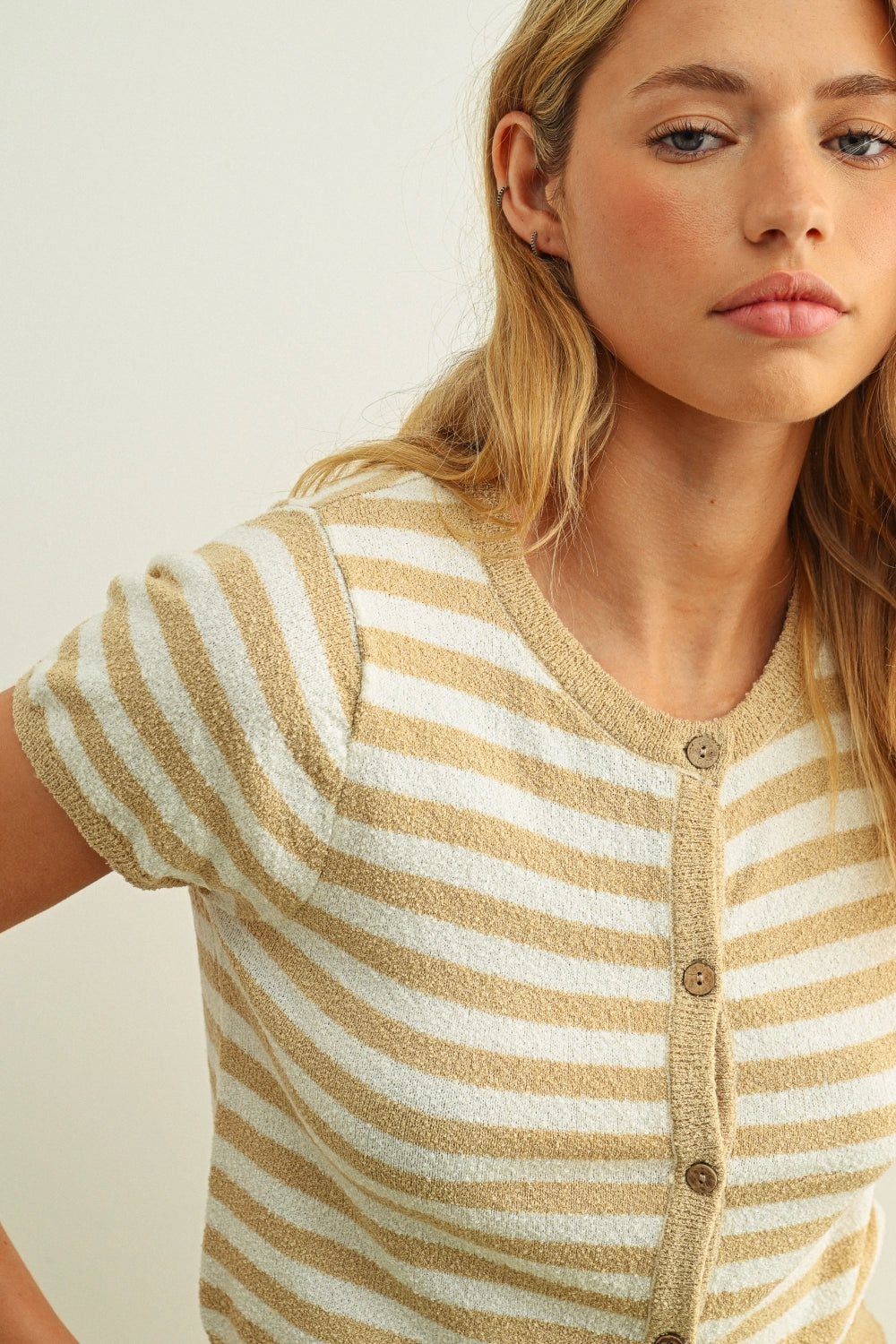 Woman wearing a beige and white striped cardigan against a plain background