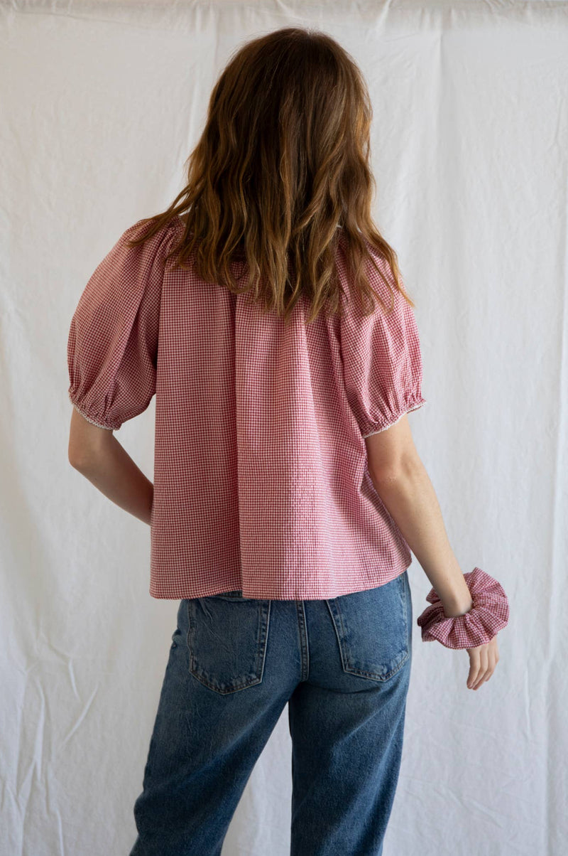 Person wearing a pink blouse and blue jeans against a white curtain background