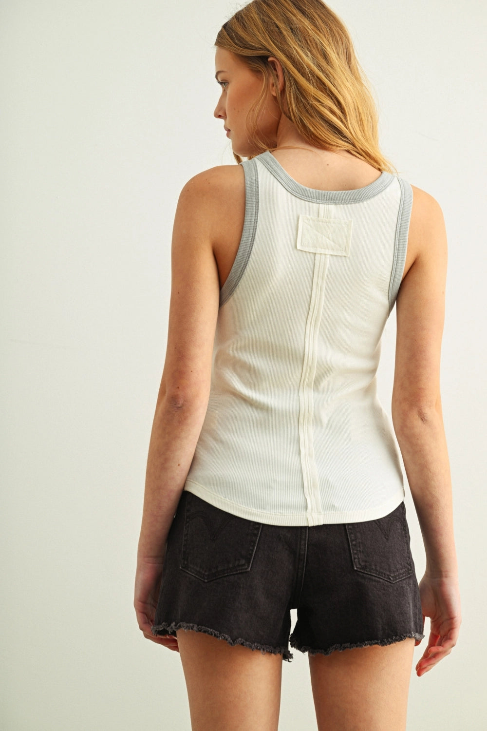 Woman wearing a white tank top with gray trim and black shorts on a plain background