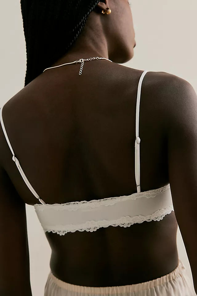 Person wearing a white lace bralette with thin straps on a neutral background