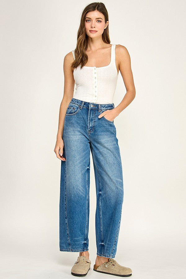 Woman wearing a white tank top and blue jeans on a plain background