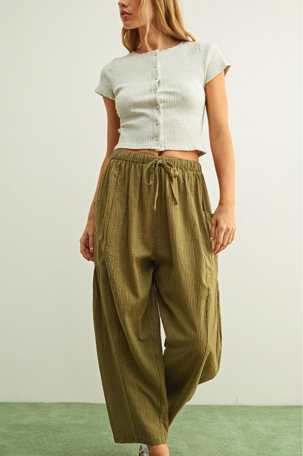 Woman wearing a white top and olive green pants on a plain background
