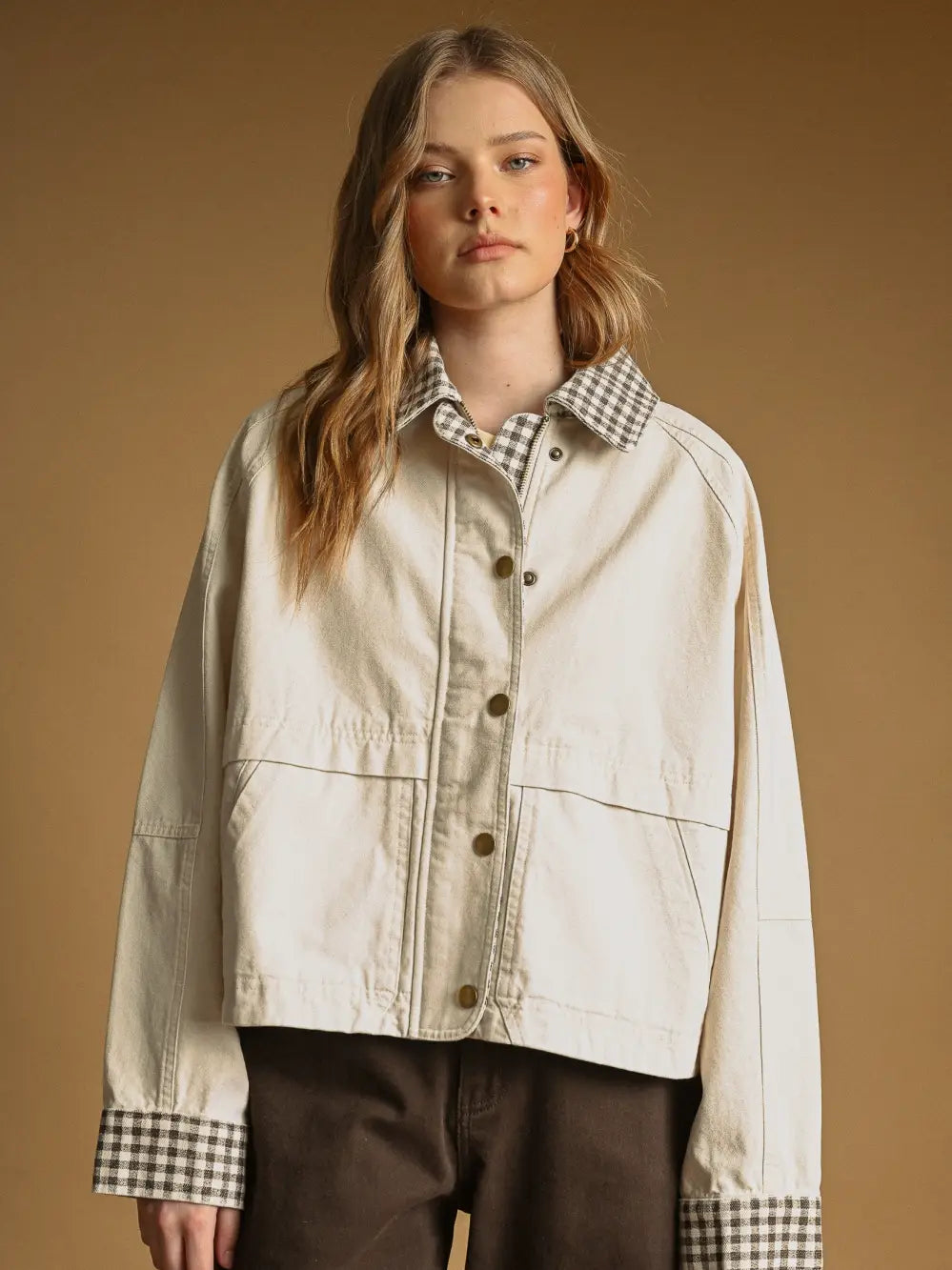 Woman wearing a beige jacket with checkered accents on a brown background