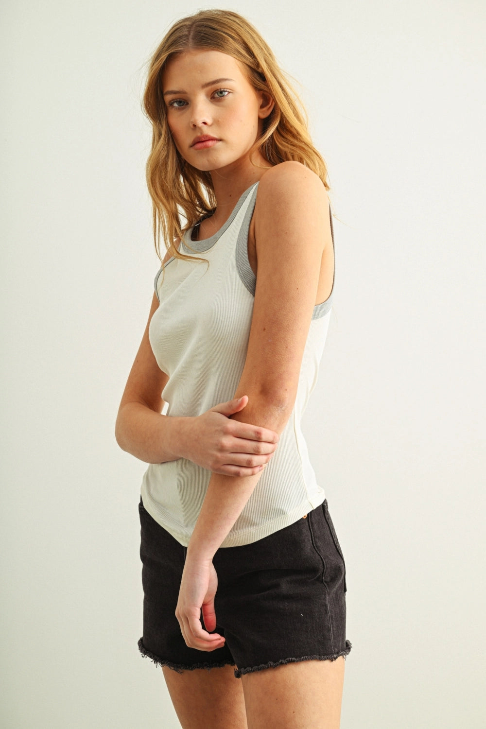 Woman wearing a white tank top and black shorts against a plain background