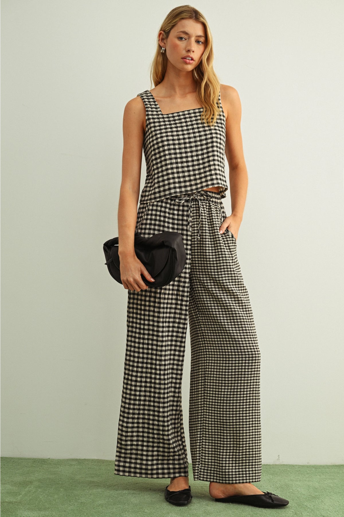 Woman wearing a black and white checkered jumpsuit holding a black handbag against a light green background