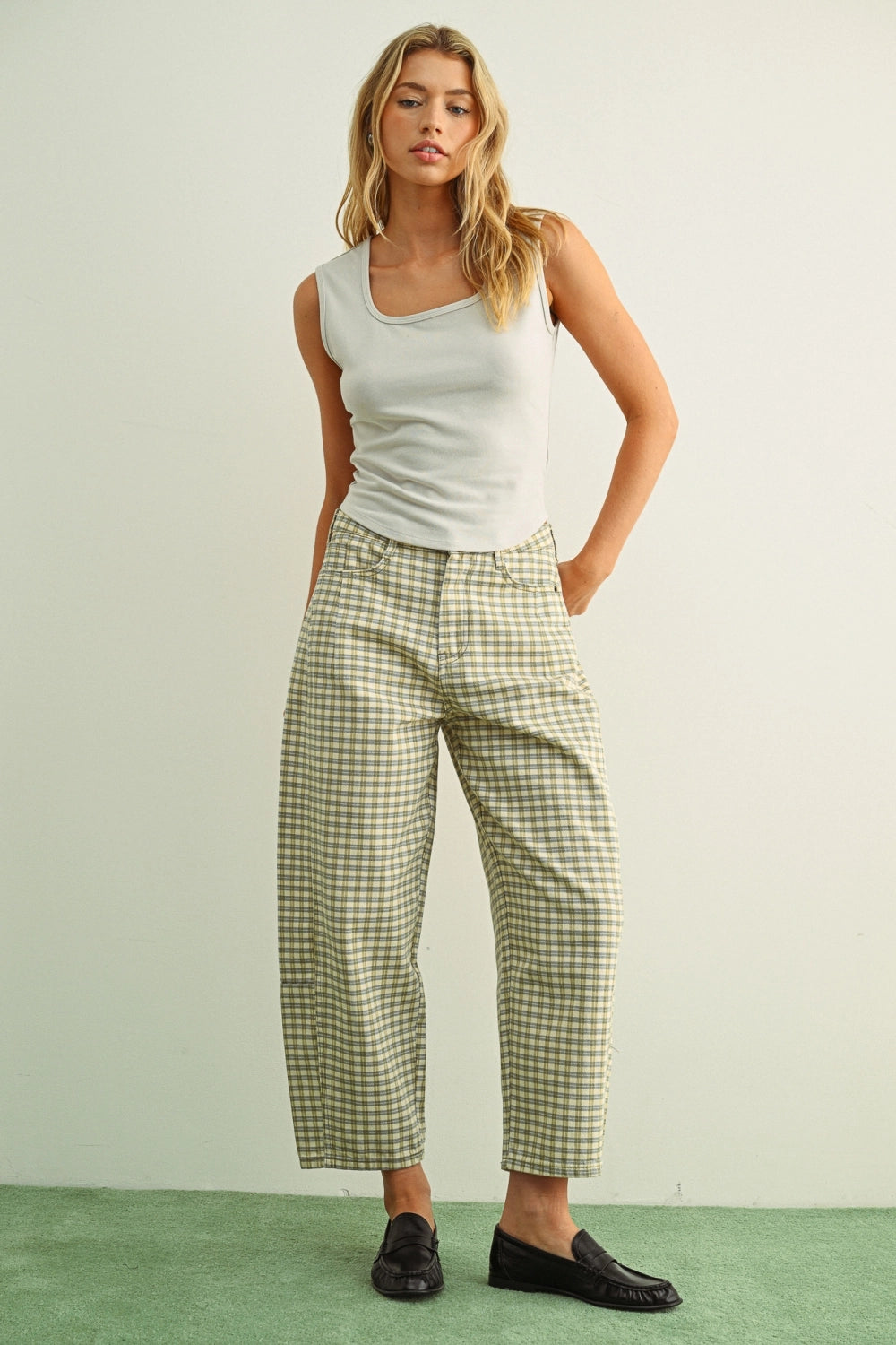 Woman wearing a white tank top and checkered pants against a light green background