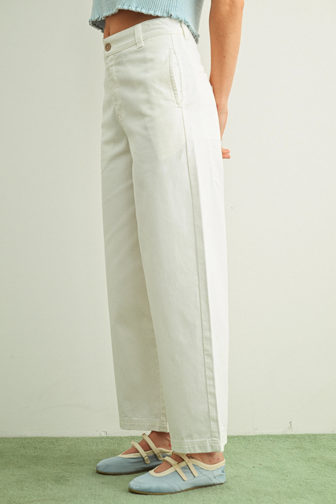 Person wearing light-colored pants and blue flats on a plain background