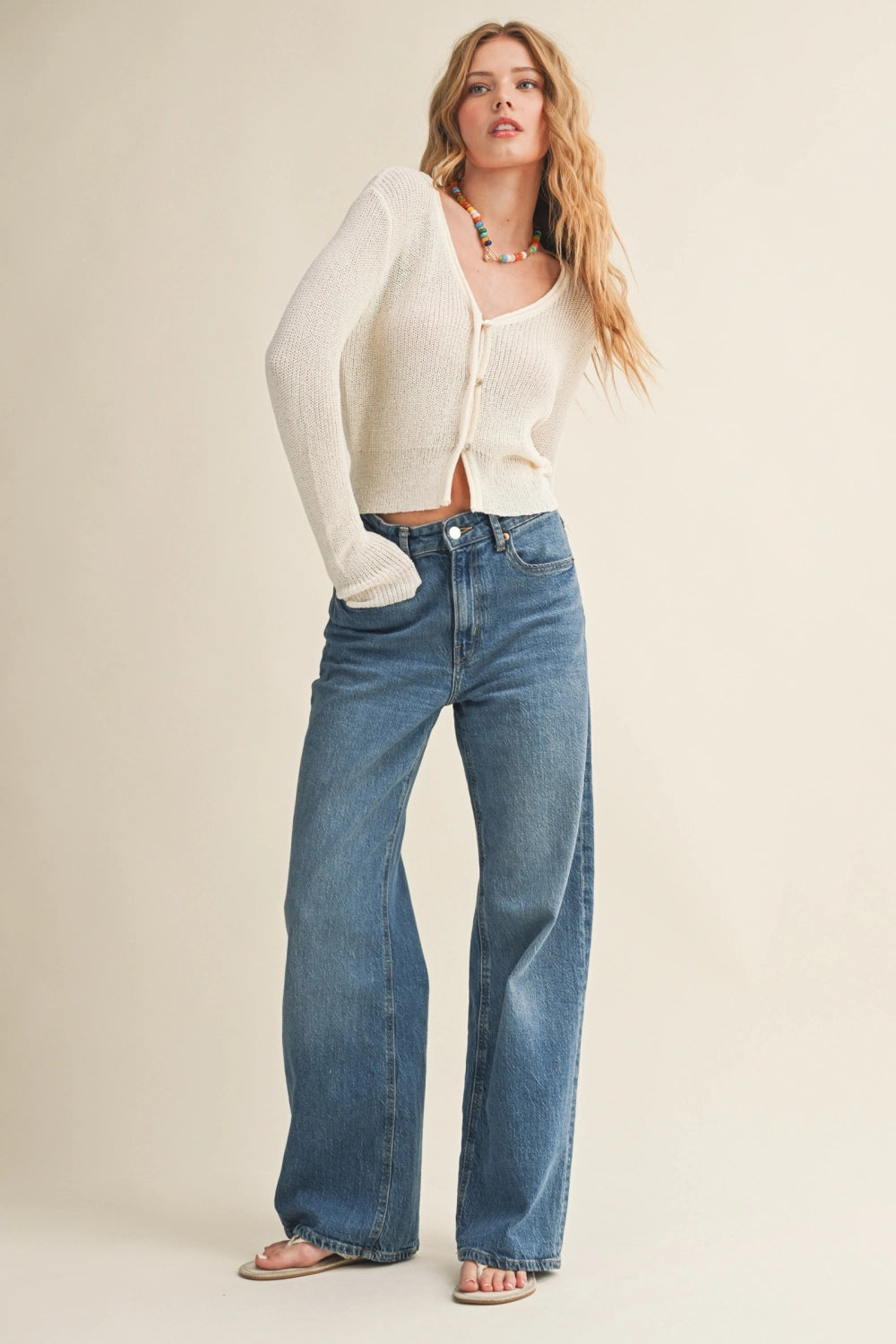 Woman wearing a white cardigan and blue jeans on a beige background