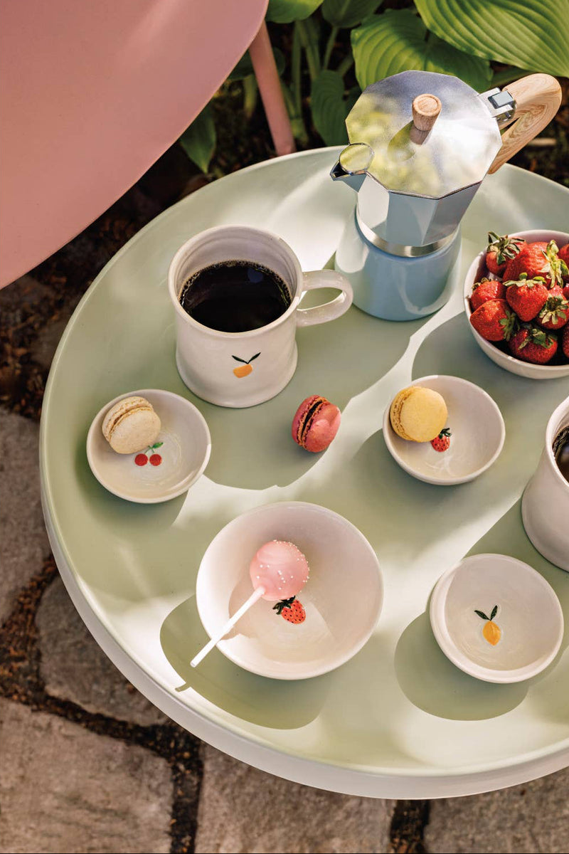 Round table with various small dishes containing pastries and a cup of coffee, set outdoors.
