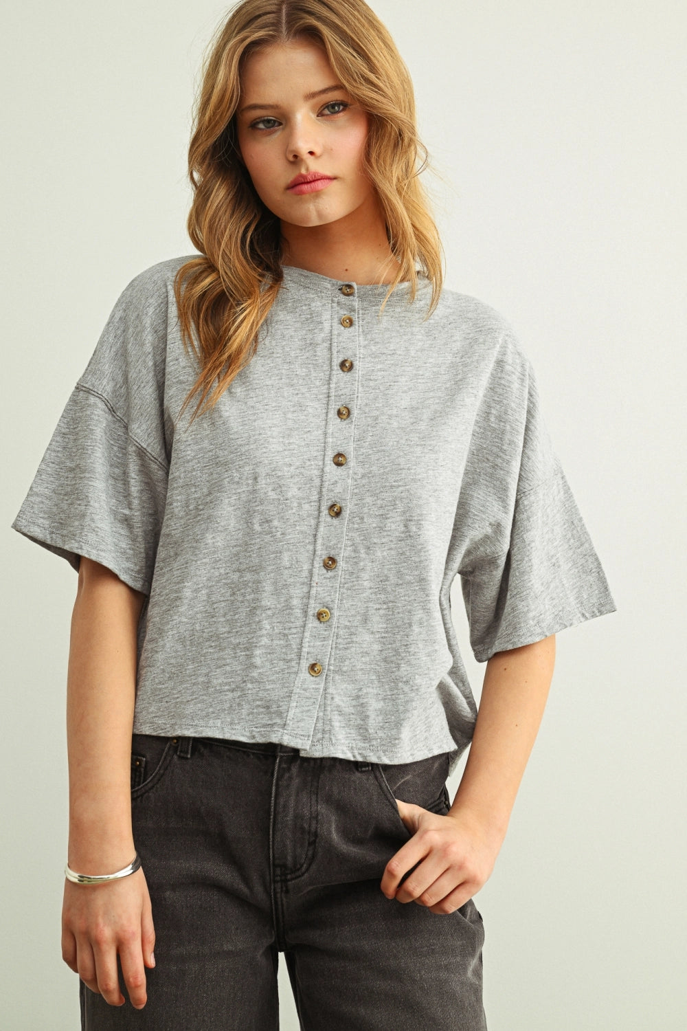 Woman wearing a grey shirt with buttons against a white background.