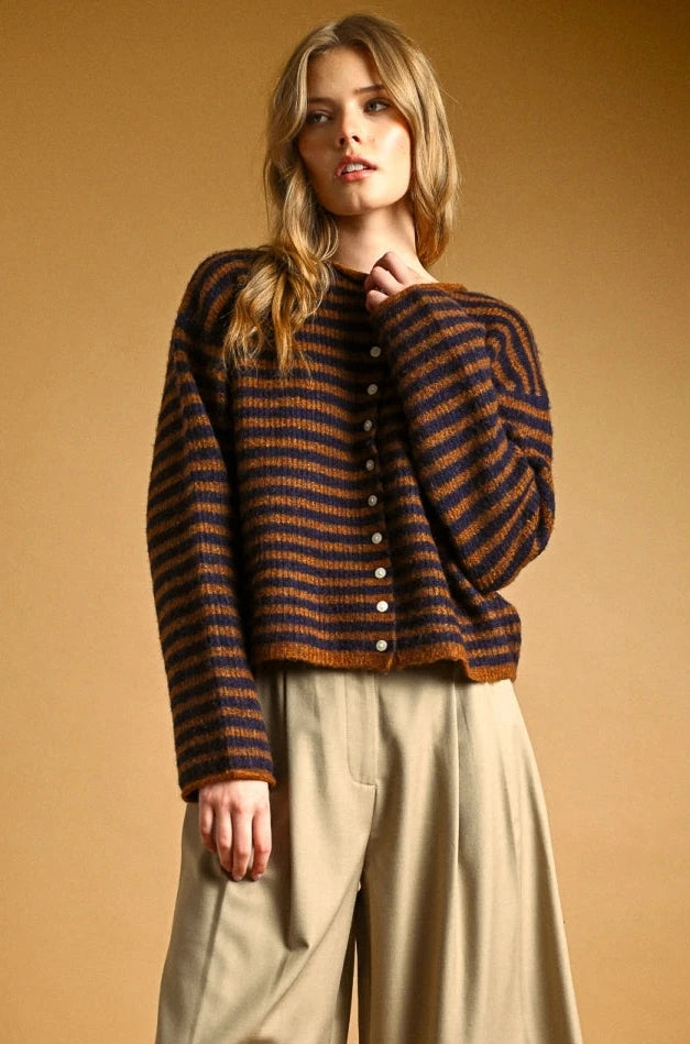 Woman wearing a striped sweater and beige pants against a brown background