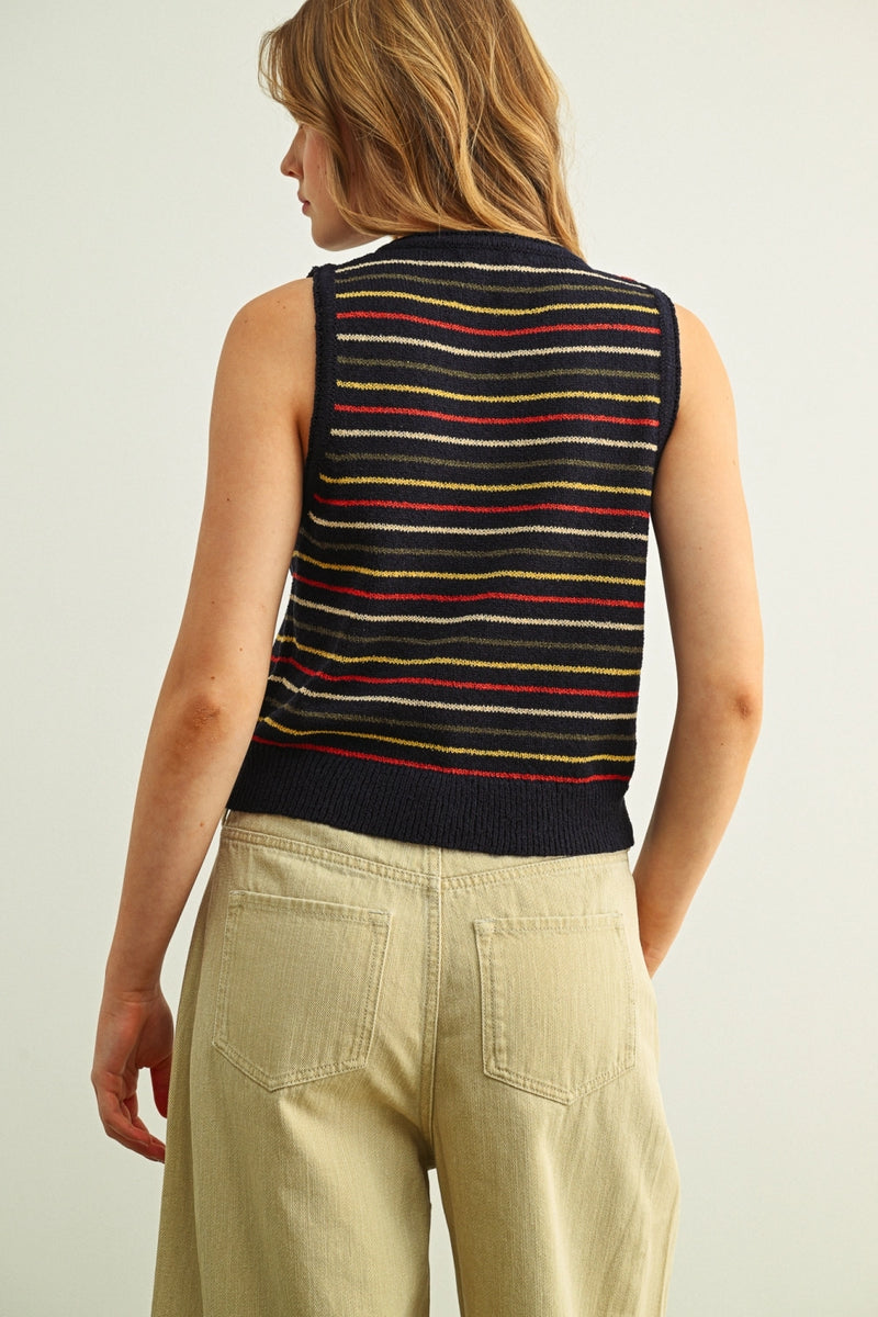 Woman wearing a striped sleeveless sweater vest and beige pants on a plain background