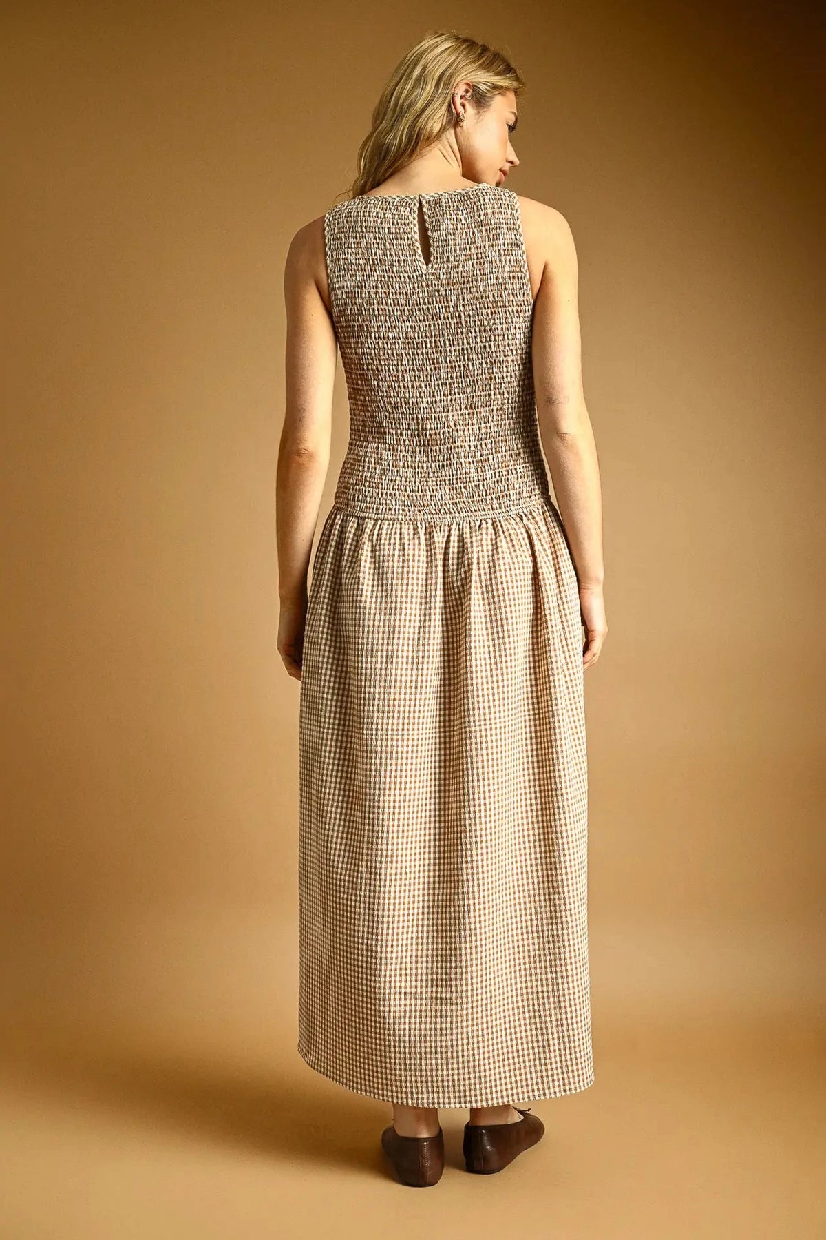 Woman wearing a sleeveless checkered dress against a beige background