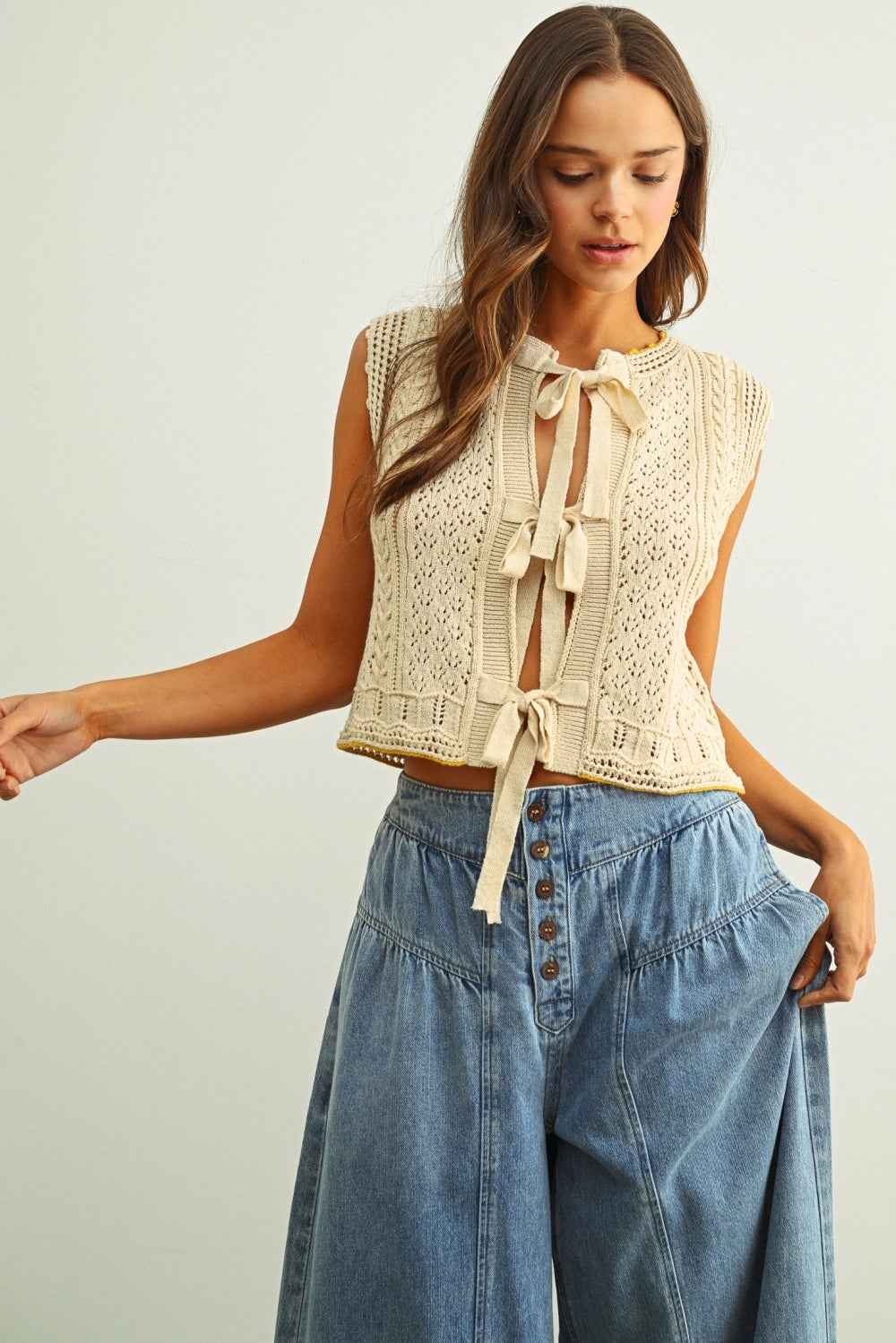 Woman wearing a beige lace top and blue denim pants on a plain background