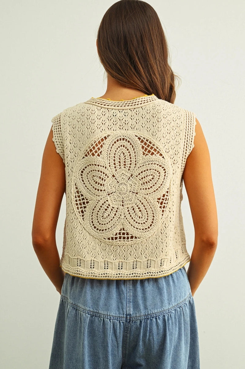 Woman wearing a beige crochet vest with a floral pattern on a plain background