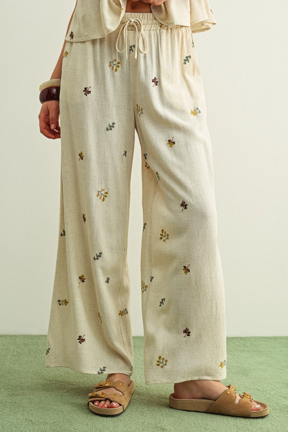 Beige pants with floral embroidery worn by a person on a green floor.