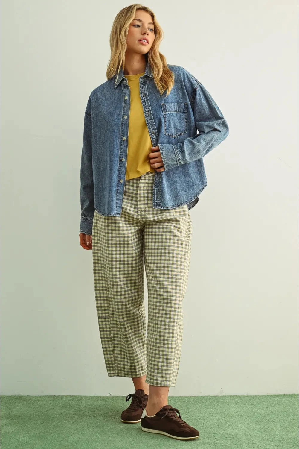 Woman wearing a denim jacket, yellow top, and plaid pants on a white background
