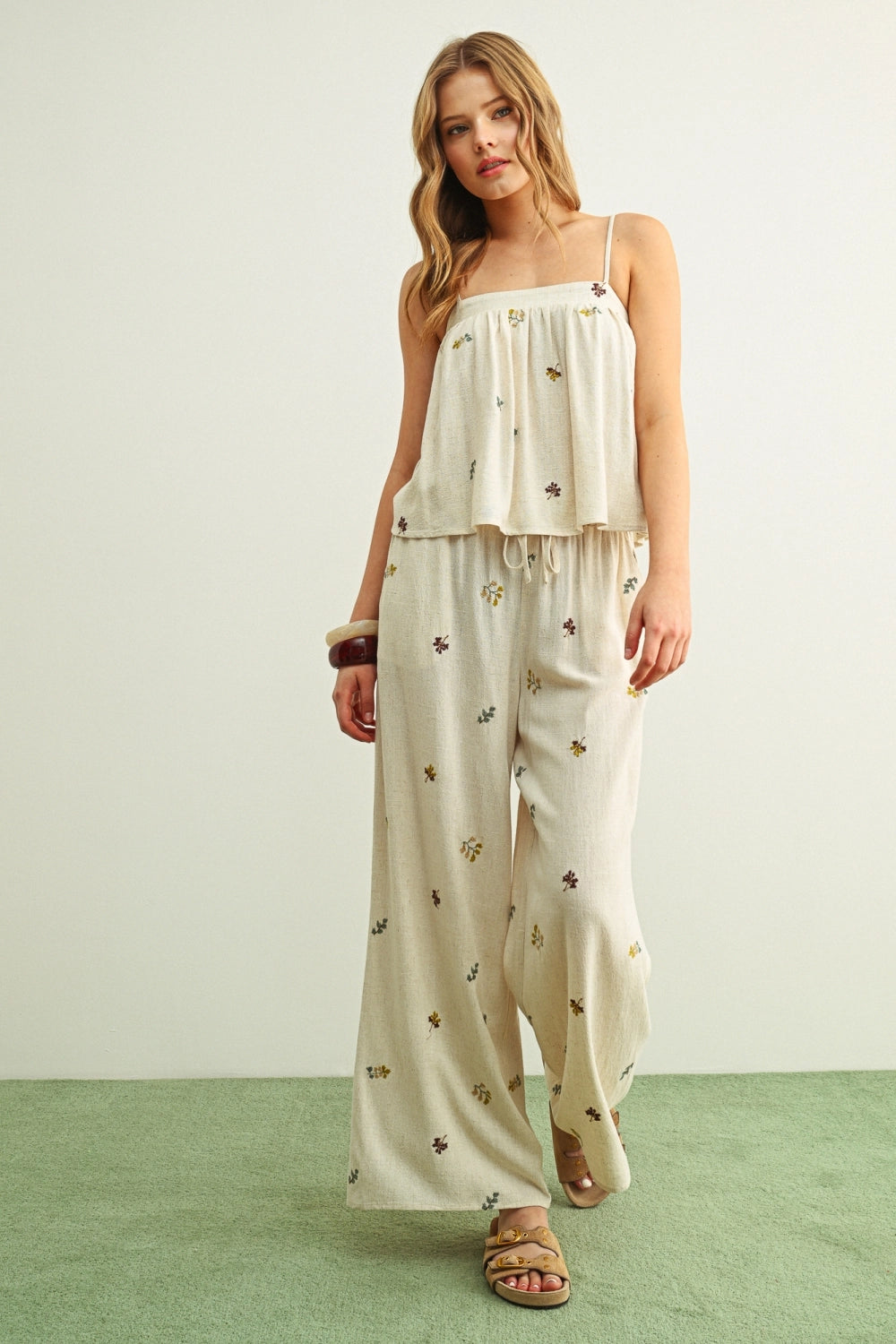 Woman wearing a beige floral dress with wide-leg pants on a white background