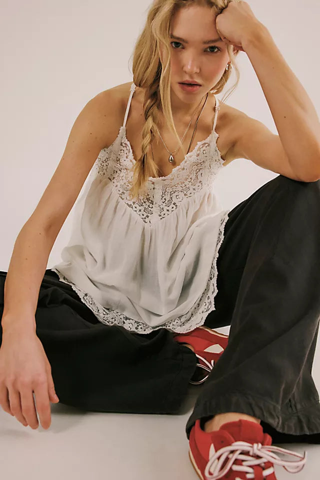 Woman wearing a white lace top and black pants sitting on the floor.
