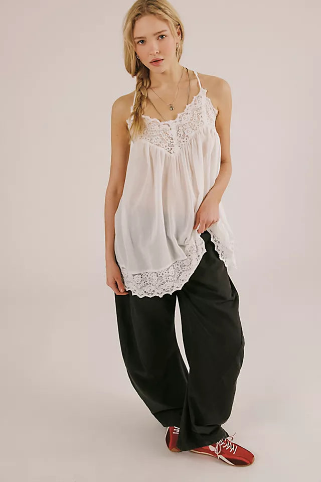 Woman wearing a white lace-trimmed top and black pants on a plain background