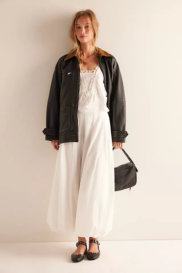 Woman wearing a black jacket over a white dress with a black handbag against a plain background